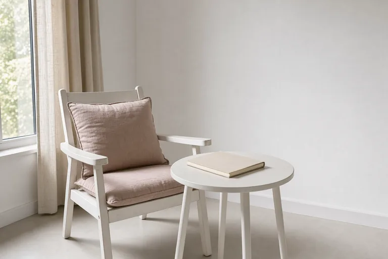 A quiet reading alcove with a white chair, pale rose cushions and afternoon light.